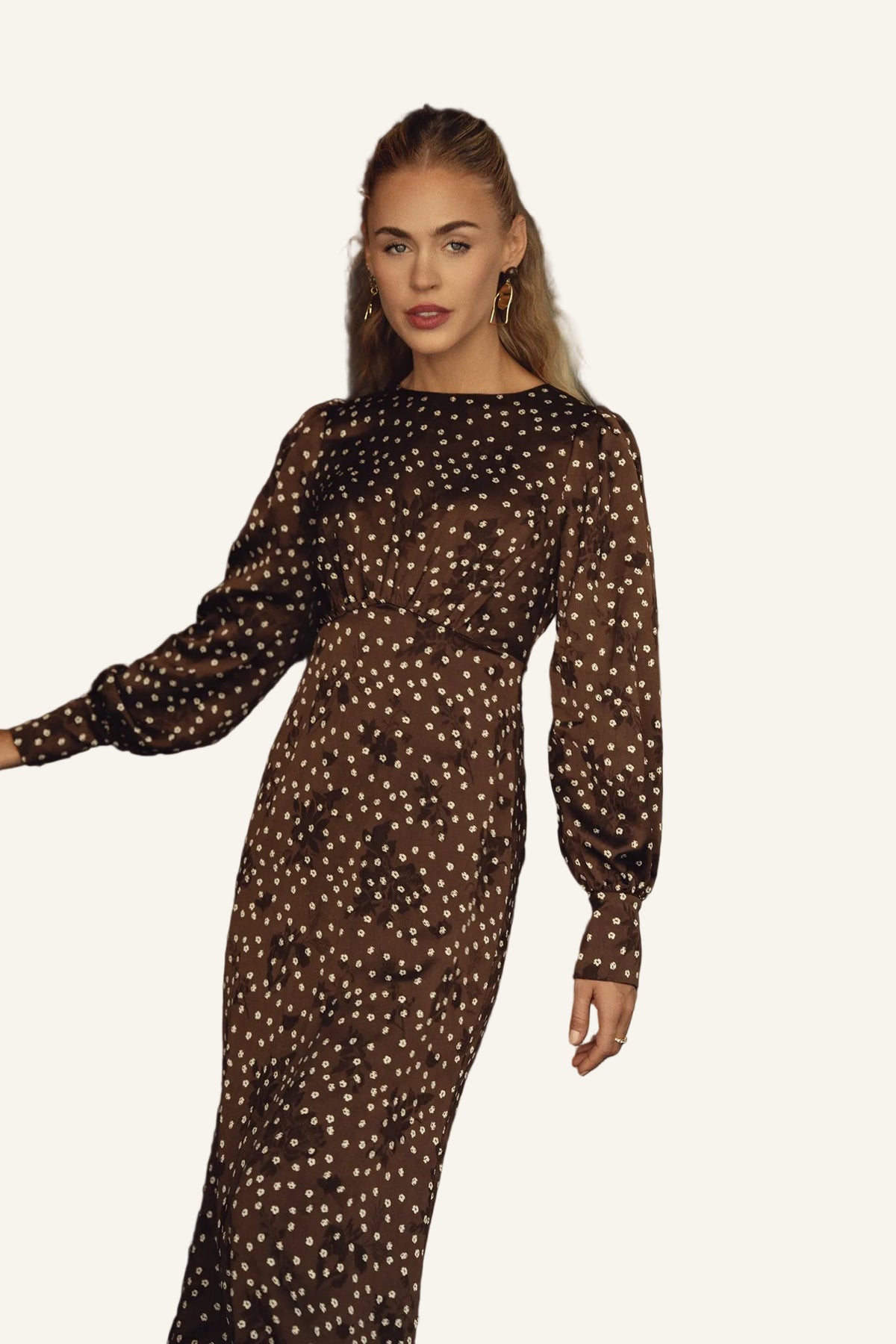 A woman wearing a long-sleeved brown maxi dress with a white polka dot pattern.