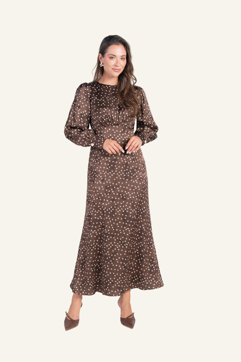 A woman modeling a long-sleeved midi dress with a brown and white polka dot pattern.