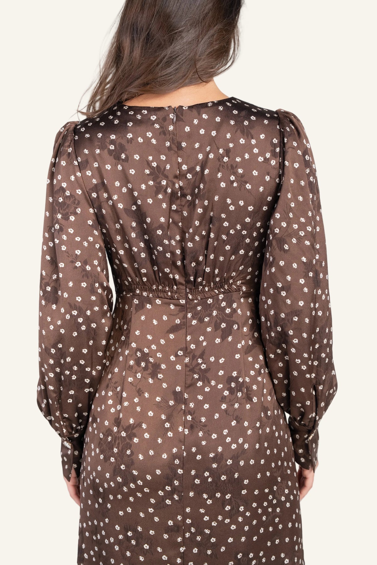 A woman viewed from the back wearing a brown long-sleeve dress with a small white floral pattern.