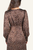 A woman viewed from the back wearing a brown long-sleeve dress with a small white floral pattern.