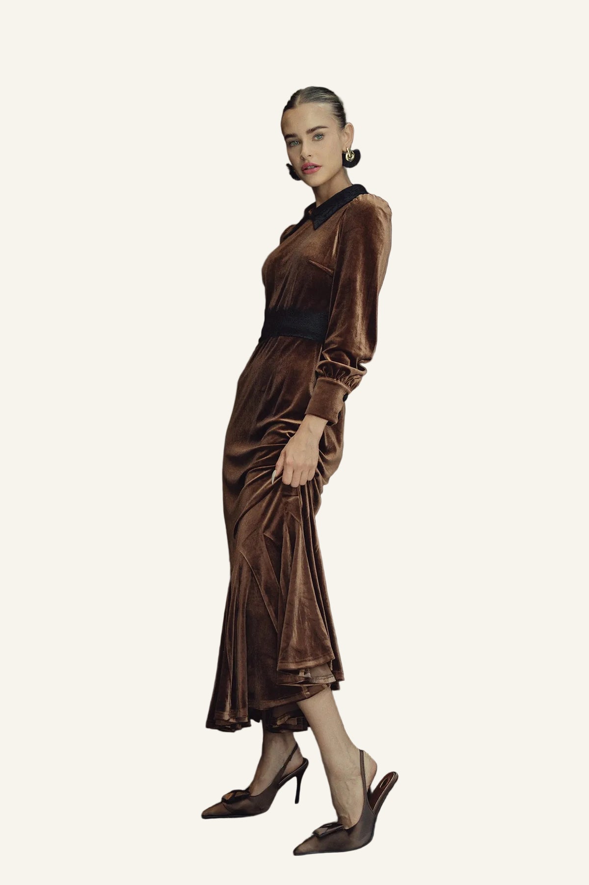 A woman models a brown velvet midi dress with a black collar and waistband, paired with brown pointed-toe heels.