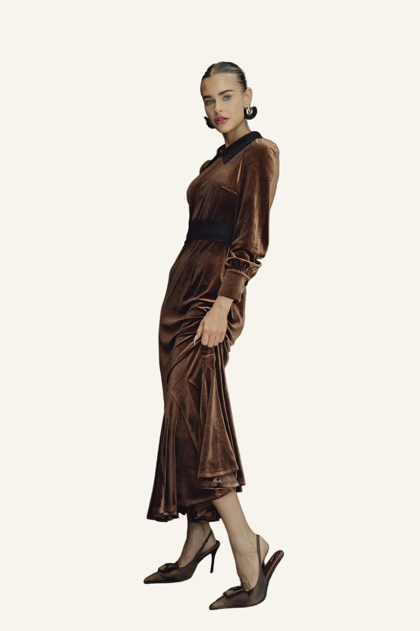 A woman models a brown velvet midi dress with a black collar and waistband, paired with brown pointed-toe heels.