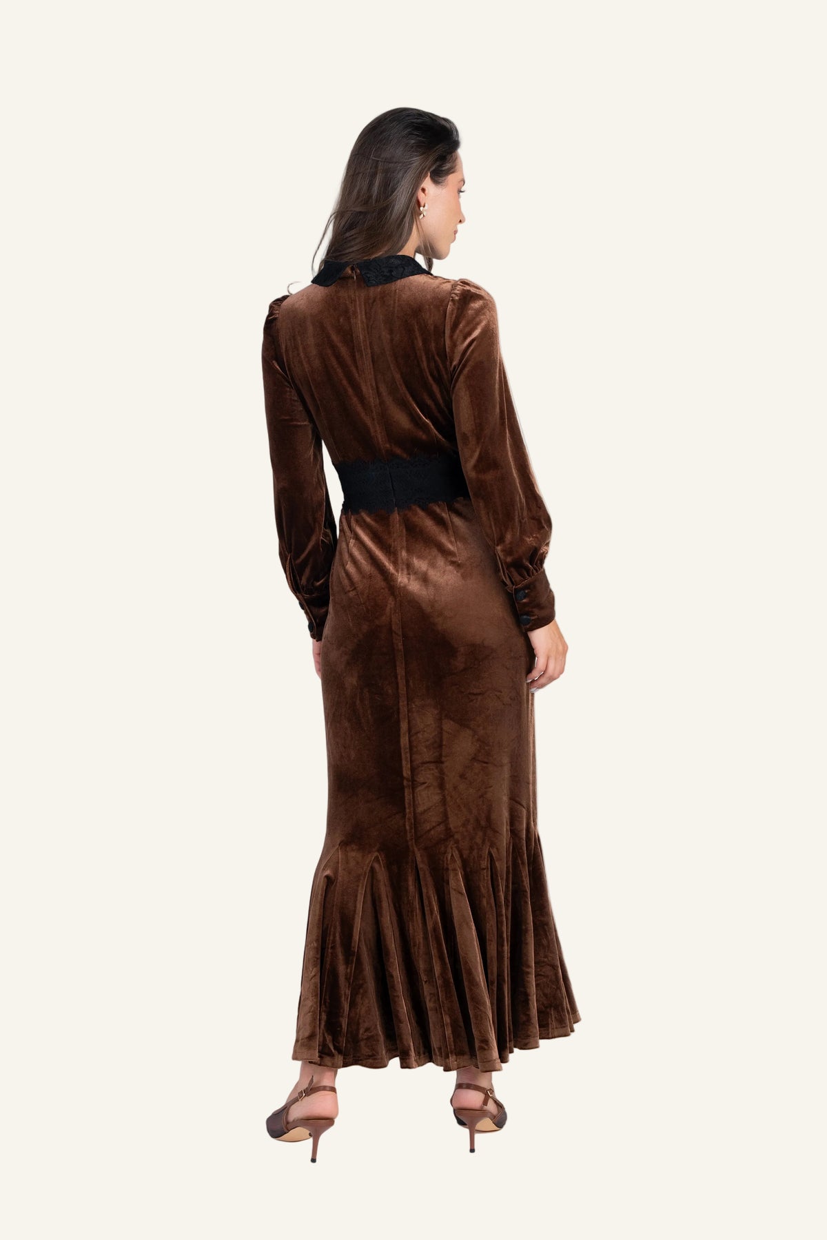 A woman wearing a long brown velvet maxi dress with a black waistband and black collar, shown from the back.