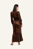 A woman wearing a long brown velvet maxi dress with a black waistband and black collar, shown from the back.