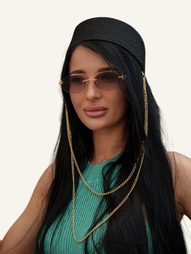 Woman wearing sunglasses and a black hat with gold chains.