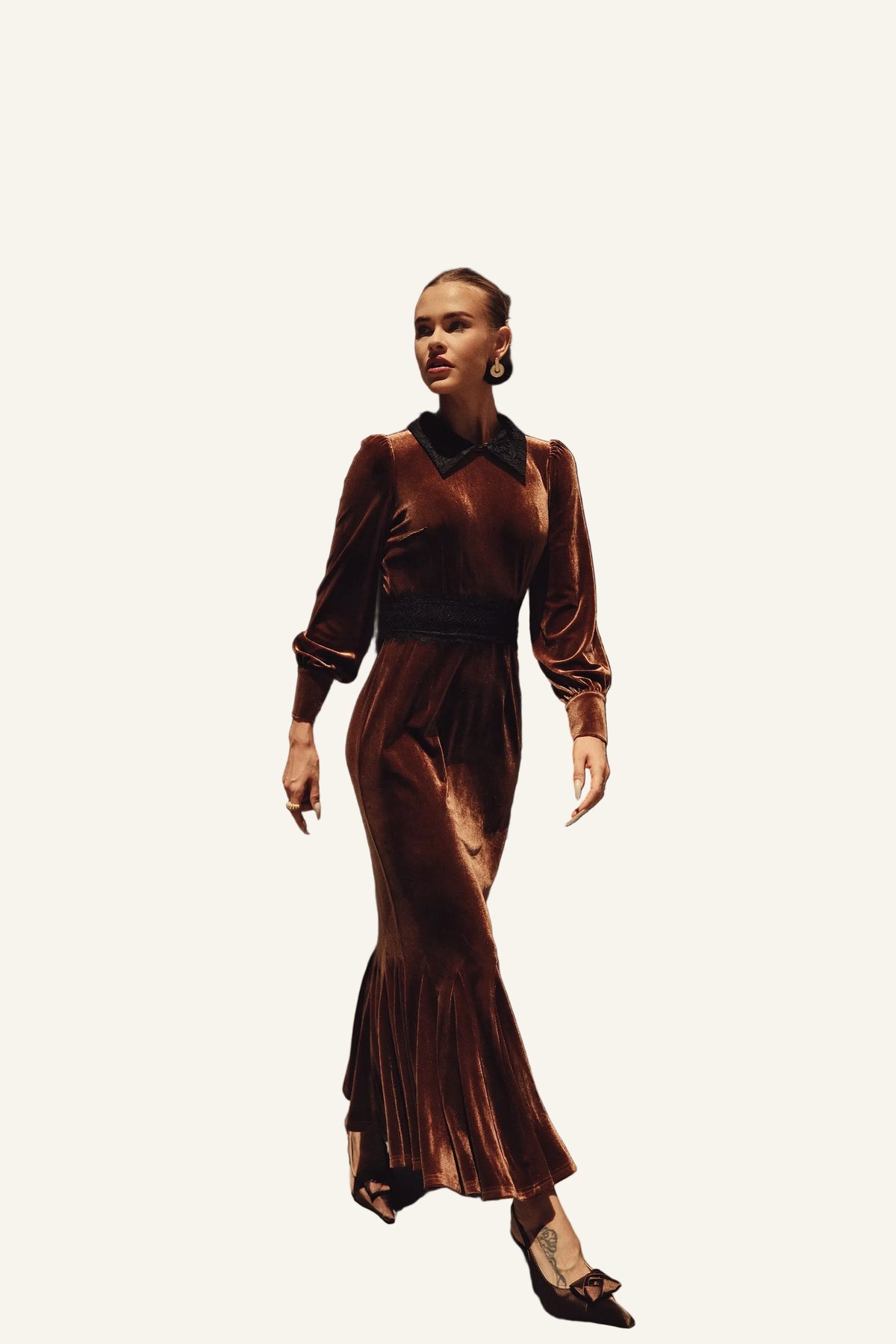 A woman wearing a long-sleeved, floor-length brown velvet dress with a black collar and waistband.