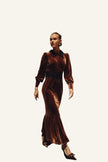 A woman wearing a long-sleeved, floor-length brown velvet dress with a black collar and waistband.