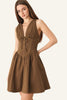 A woman modeling a sleeveless brown mini dress with a deep V-neckline, gathered bust, and flared skirt against a plain light gray studio background.