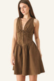 A woman modeling a sleeveless brown mini dress with a deep V-neckline, gathered bust, and flared skirt against a plain light gray studio background.