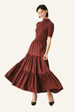 A woman modeling a rust-brown tiered midi dress with short sleeves and a mock neck, paired with black pointed-toe heels.