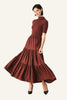 A woman modeling a rust-brown tiered midi dress with short sleeves and a mock neck, paired with black pointed-toe heels.