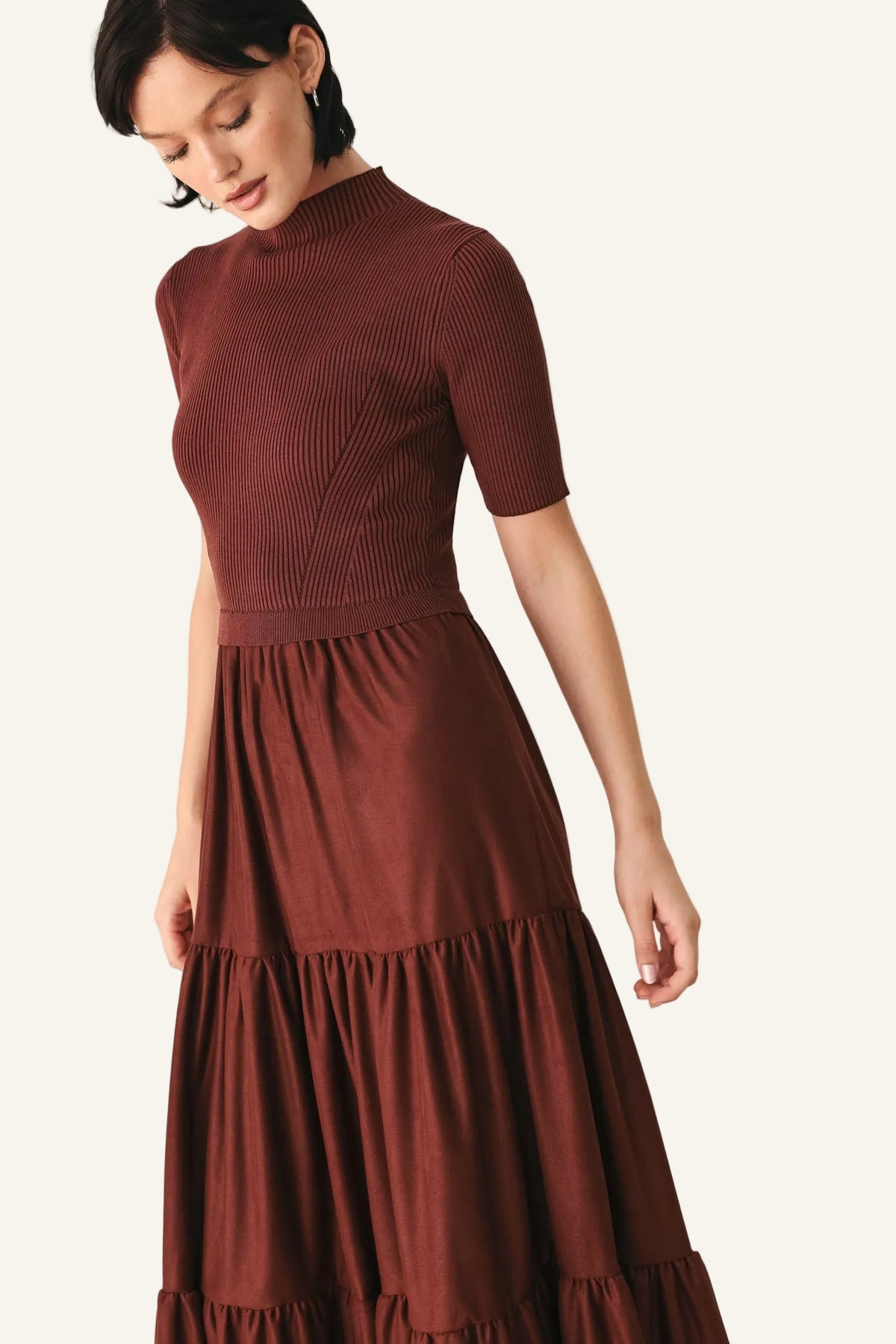 A woman wearing a rust-brown ribbed short-sleeve mock-neck dress with a tiered skirt.