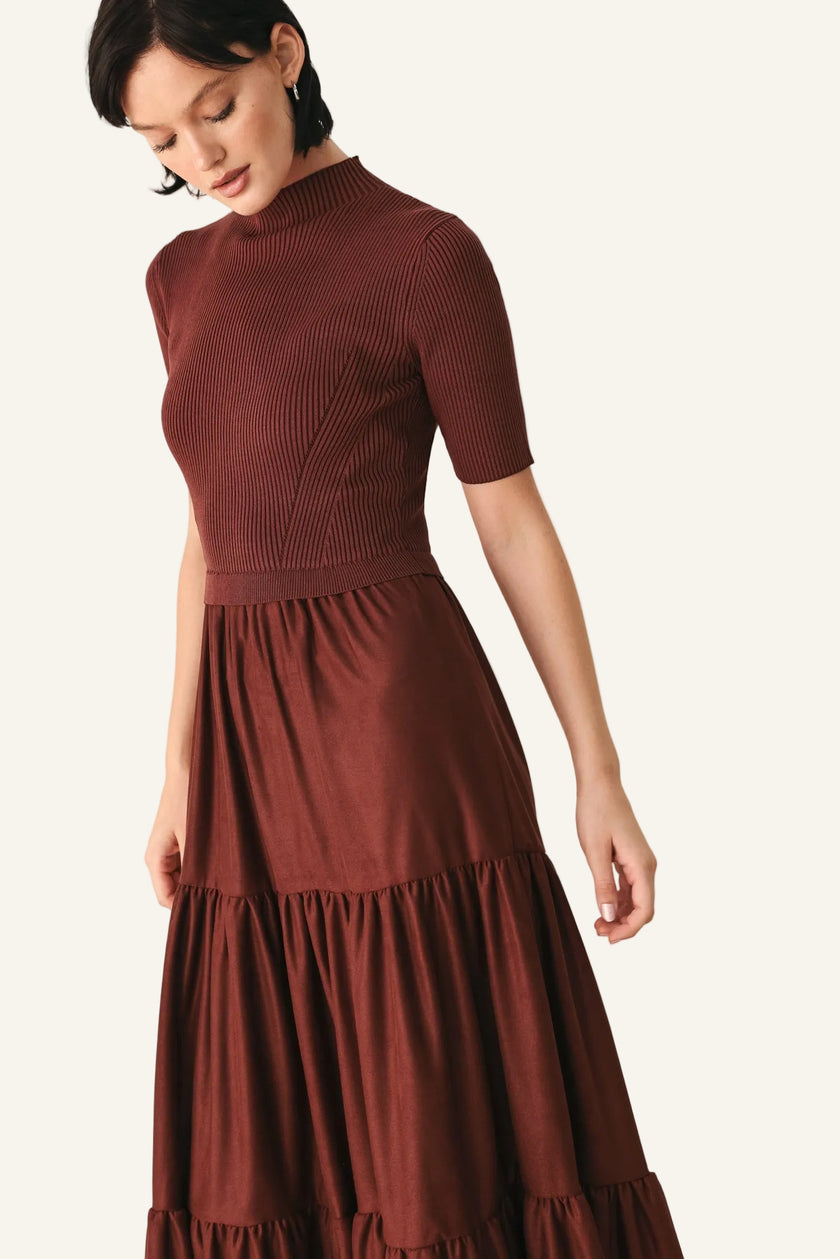 A woman wearing a rust-brown ribbed short-sleeve mock-neck dress with a tiered skirt.