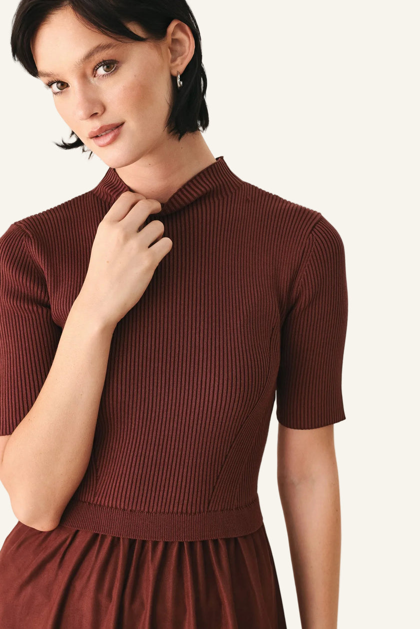 A woman wearing a ribbed short-sleeve mock neck dress in a deep rust brown color.