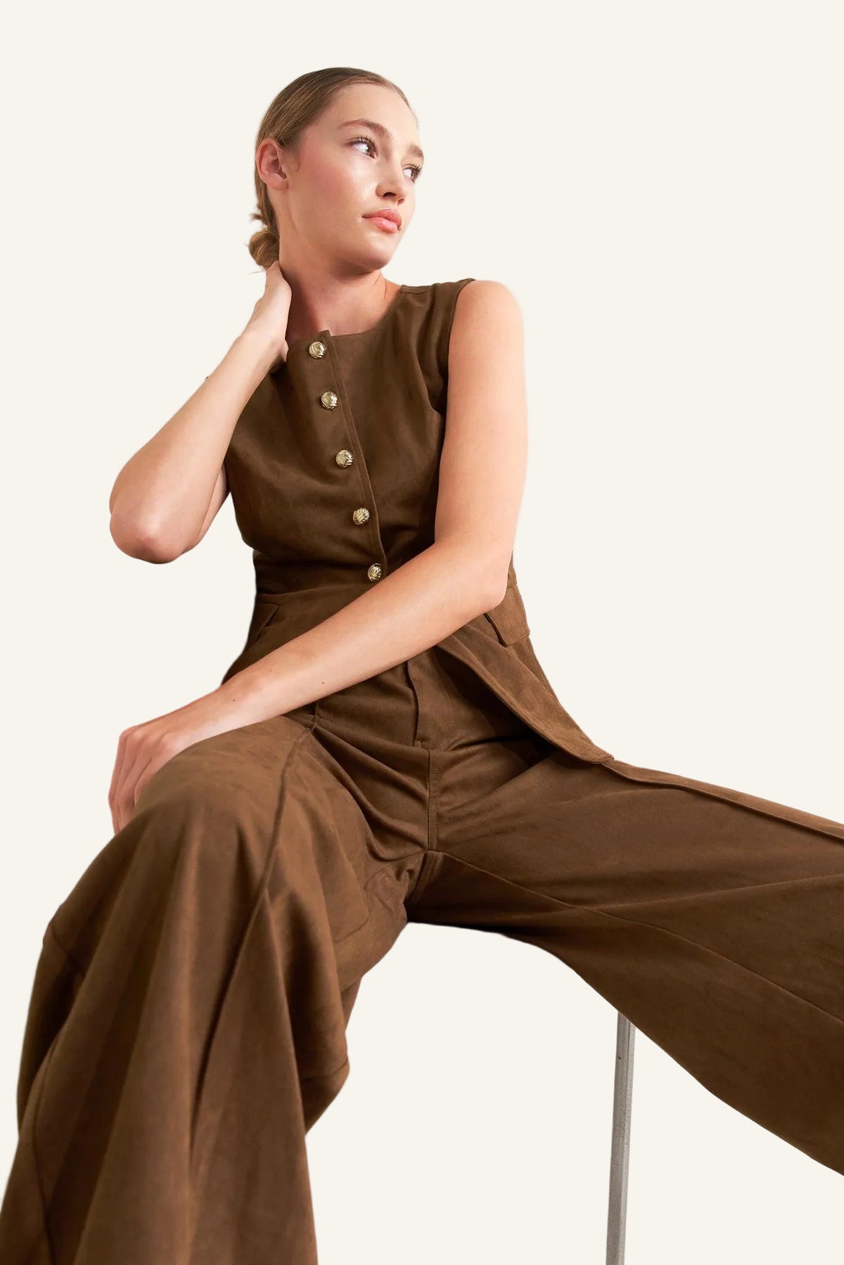 Woman wearing a brown top and brown bottoms sitting on a chair against a white background