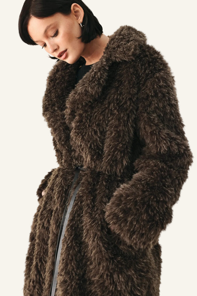 A model wearing a dark brown shaggy faux fur coat with a matching belt, photographed against a plain light background.
