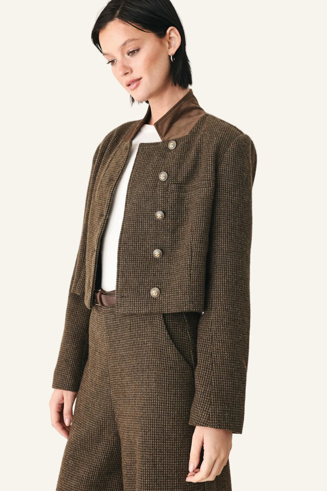 A model wearing a brown and black micro-check cropped jacket with a high collar and silver buttons, paired with matching brown trousers and a white top.