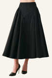 A black high-waisted A-line midi skirt with pleated detailing, shown on a model wearing black pointed-toe stiletto heels against a light gray studio background.