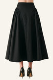 A black high-waisted A-line midi skirt with dramatic gathered side pleats, shown from the back on a model wearing black pointed-toe heels against a light gray studio background.