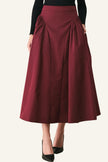 A woman wearing a high-waisted, pleated midi skirt in deep burgundy, paired with a black long-sleeve top and black pointed-toe heels, standing against a light gray studio background.