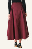 A model from the waist down wearing a high-waisted, pleated A-line midi skirt in burgundy, paired with a black long-sleeve top and black high heels.