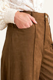 Brown pants with a hand adjusting the waistband against a neutral background