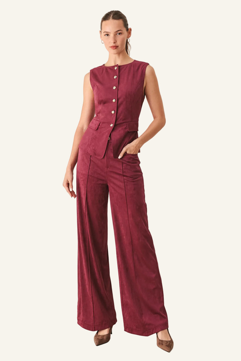 A woman modeling a sleeveless burgundy top with a buttoned neckline and wide-leg pants.