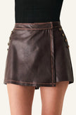 A dark brown faux-leather mini skirt with asymmetrical button details on the sides, worn by a model with a black ribbed top visible at the waist.