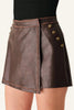 A close-up of a model wearing a dark brown faux-leather wrap mini skirt with gold-tone decorative buttons on the side, paired with a black ribbed top.