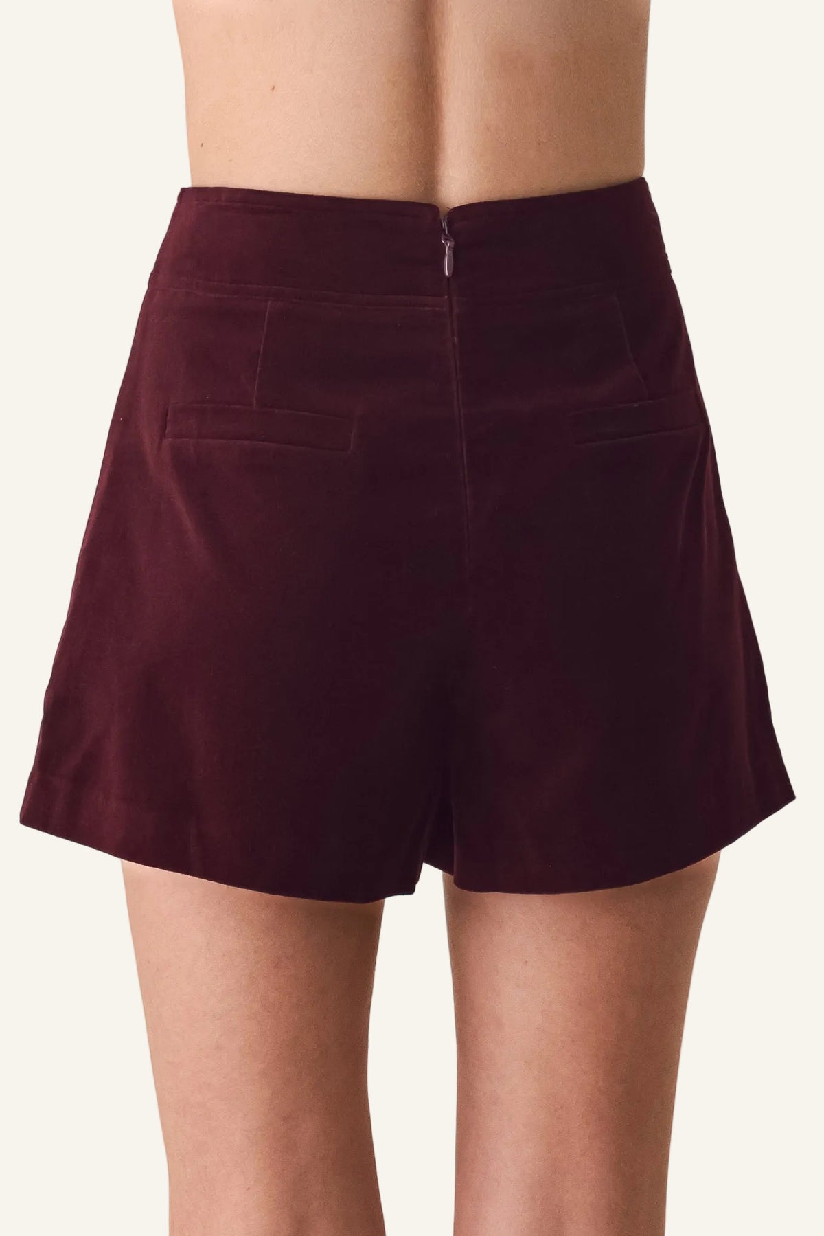 A person wearing high-waisted burgundy velvet shorts, shown from the back against a plain off-white background.