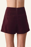 A person wearing high-waisted burgundy velvet shorts, shown from the back against a plain off-white background.