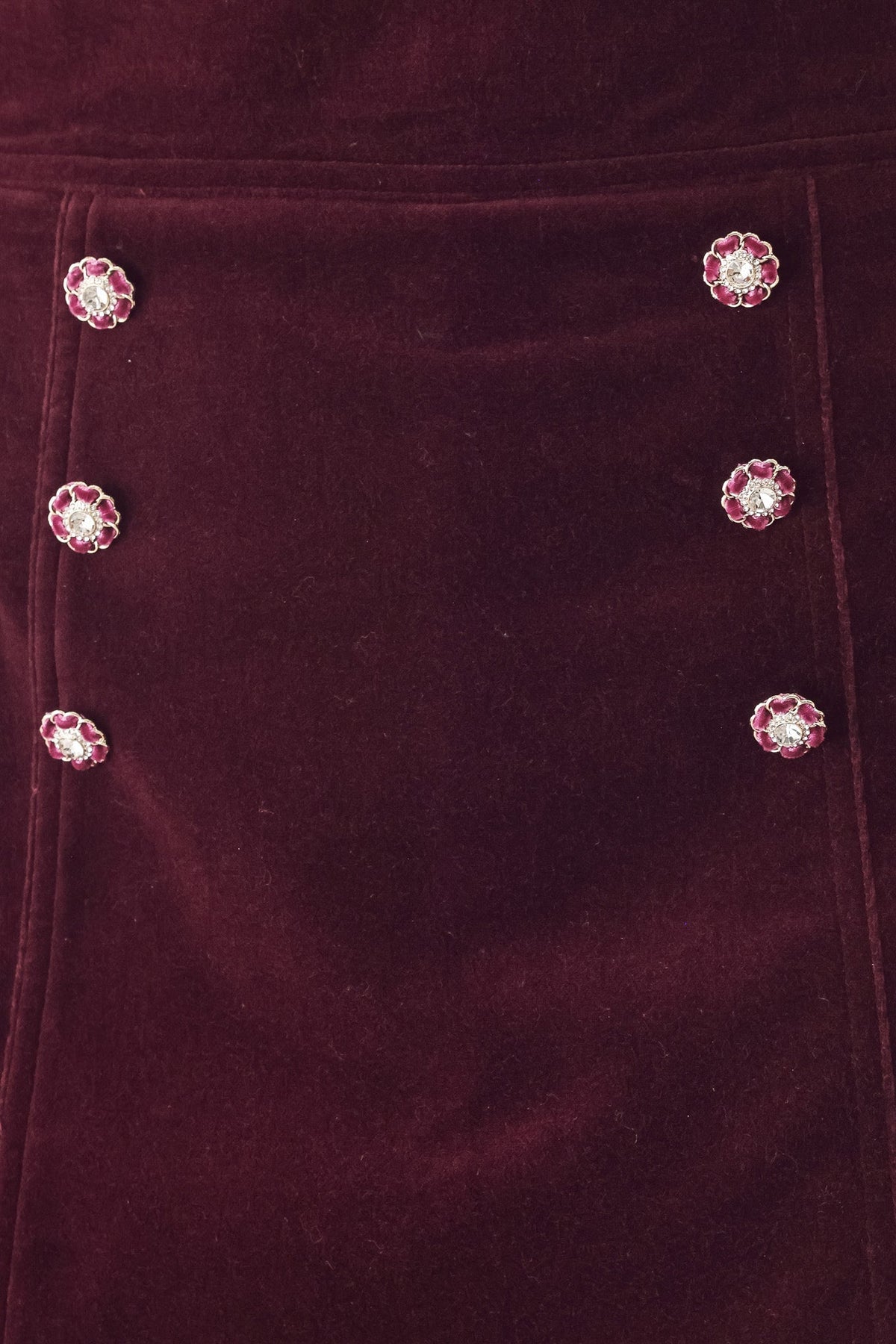 Close-up of a deep burgundy velvet fabric with decorative floral embellishments featuring pink petals and clear rhinestones, arranged in two vertical columns.