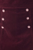 Close-up of a deep burgundy velvet fabric with decorative floral embellishments featuring pink petals and clear rhinestones, arranged in two vertical columns.