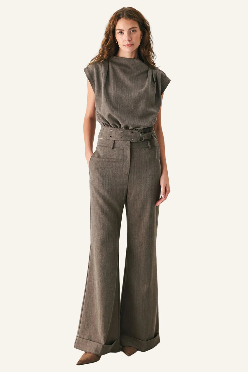 A woman modeling a matching two-piece outfit consisting of a short-sleeve, high-neck, textured taupe top and matching high-waisted wide-leg trousers with a matching belt, set against a plain white studio background.