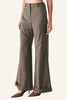A model is wearing a pair of high-waisted, wide-leg trousers in a textured taupe-brown fabric, paired with brown pointed-toe heels, against a plain light gray studio background.