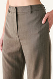 Close-up of a person wearing olive brown wide-leg trousers, showing the front waistband, side pocket, and hand in the pocket against a plain light background.