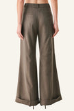 A model shown from the back wearing high-waisted, wide-leg trousers in a textured taupe-brown fabric, styled with black heels against a plain white studio background.