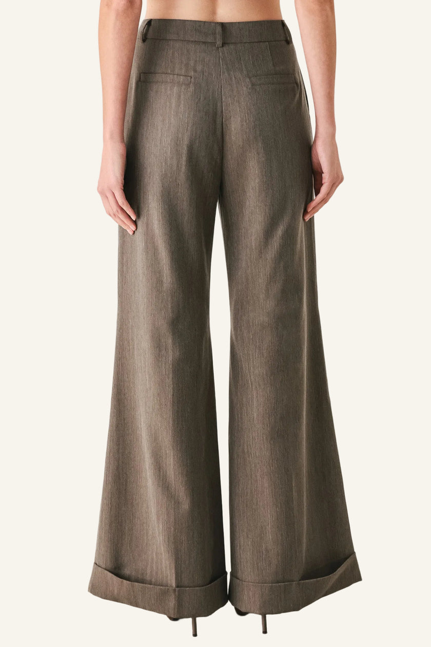 A model shown from the back wearing high-waisted, wide-leg trousers in a textured taupe-brown fabric, styled with black heels against a plain white studio background.