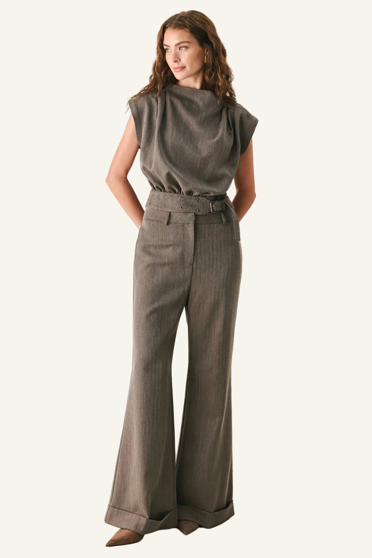 A woman modeling a two-piece outfit consisting of a muted olive-brown sleeveless top and matching high-waisted, wide-leg trousers with a belt, set against a plain light gray studio background.