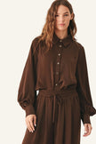 A woman wearing a dark brown long-sleeve button-up shirt and matching brown drawstring skirt.