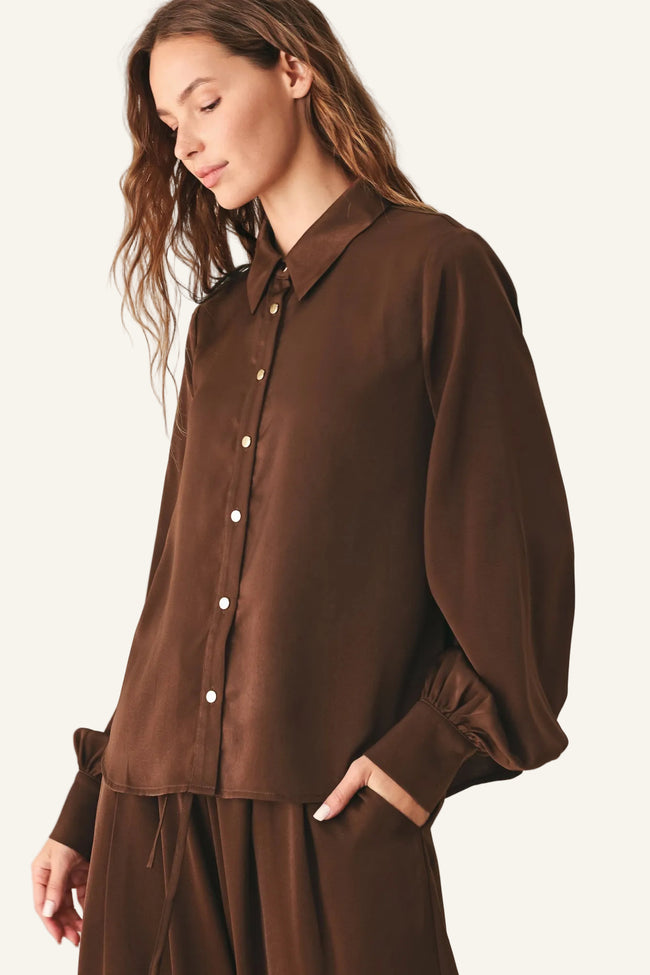 A woman wearing a brown button-up shirt with balloon sleeves and matching brown bottoms.