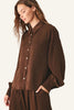 A woman wearing a brown button-up shirt with balloon sleeves and matching brown bottoms.