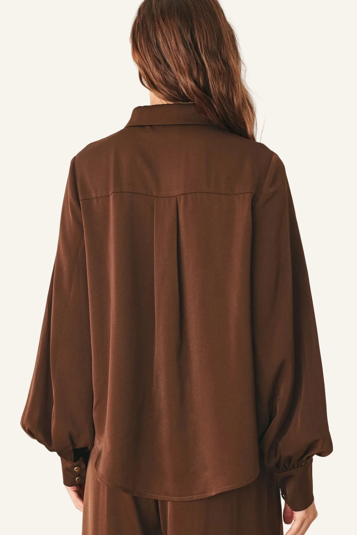 A woman viewed from the back wearing a brown long-sleeve blouse with balloon sleeves and matching brown pants.