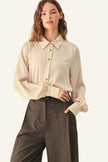 A woman modeling a cream-colored long-sleeve button-up blouse with gathered cuffs, paired with dark brown wide-leg trousers.