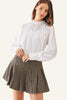 A woman wearing a white long-sleeve blouse with pleated detailing and a brown and beige houndstooth mini skirt.