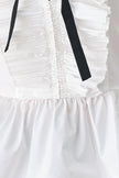 Close-up of a white ruffled garment with a gathered center front and two black ribbon ties hanging down the bodice.
