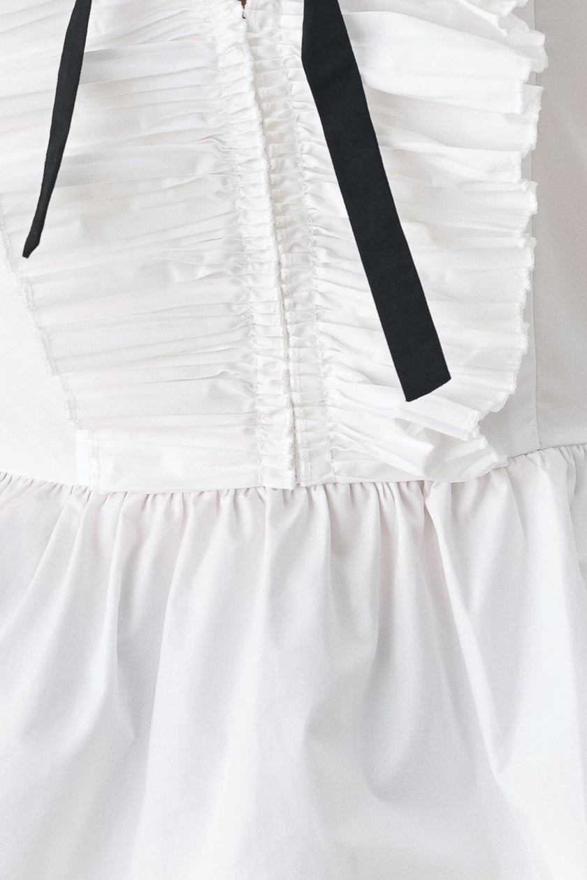 Close-up of a white ruffled garment with a gathered center front and two black ribbon ties hanging down the bodice.