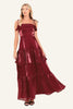 A woman modeling a sleeveless, tiered maxi dress in a shiny deep burgundy fabric.