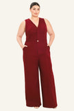 A woman modeling a sleeveless burgundy wide-leg jumpsuit with a V-neckline and front button detail, photographed against a plain light beige studio background.