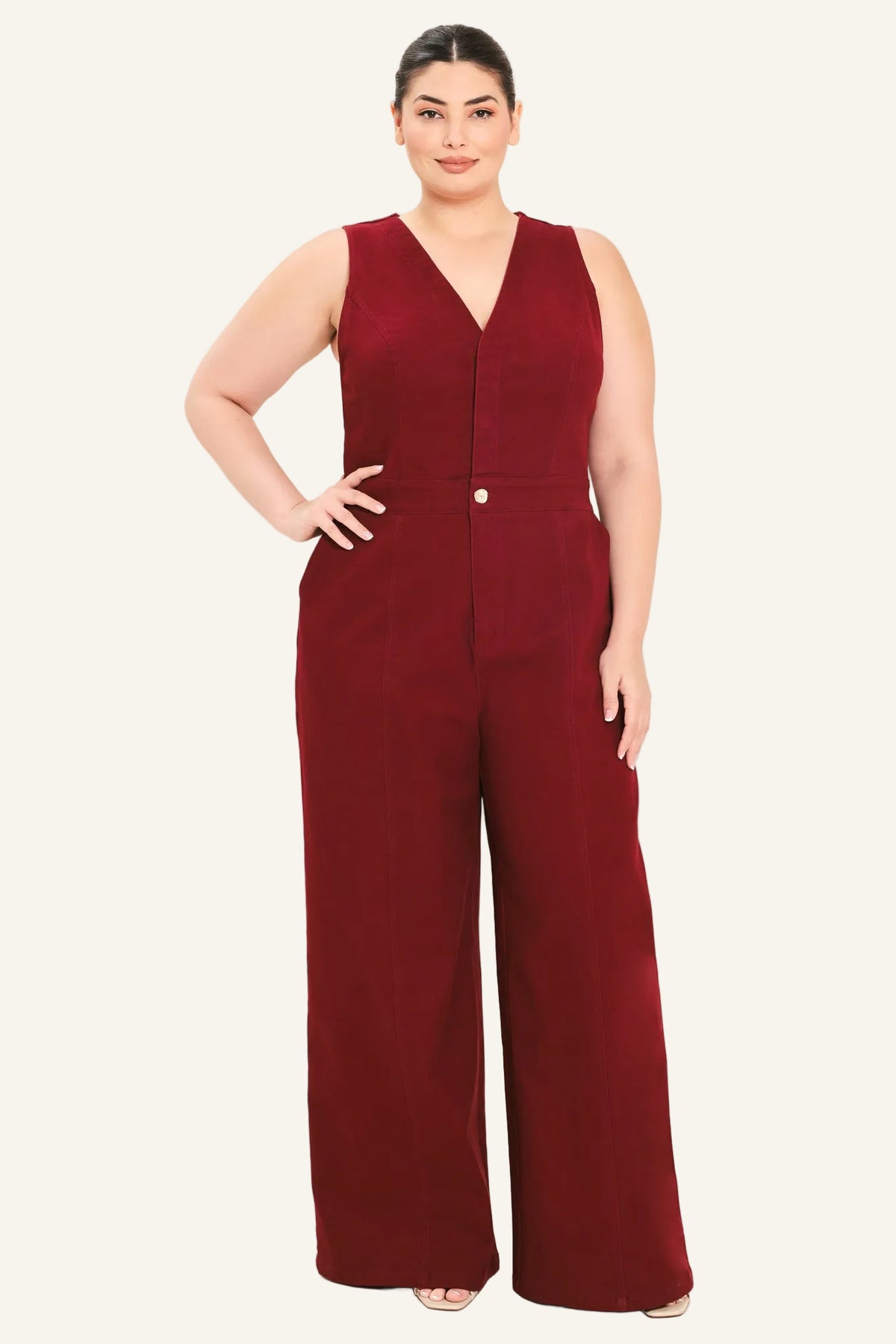 A woman modeling a sleeveless burgundy wide-leg jumpsuit with a V-neckline and front button detail, photographed against a plain light background.